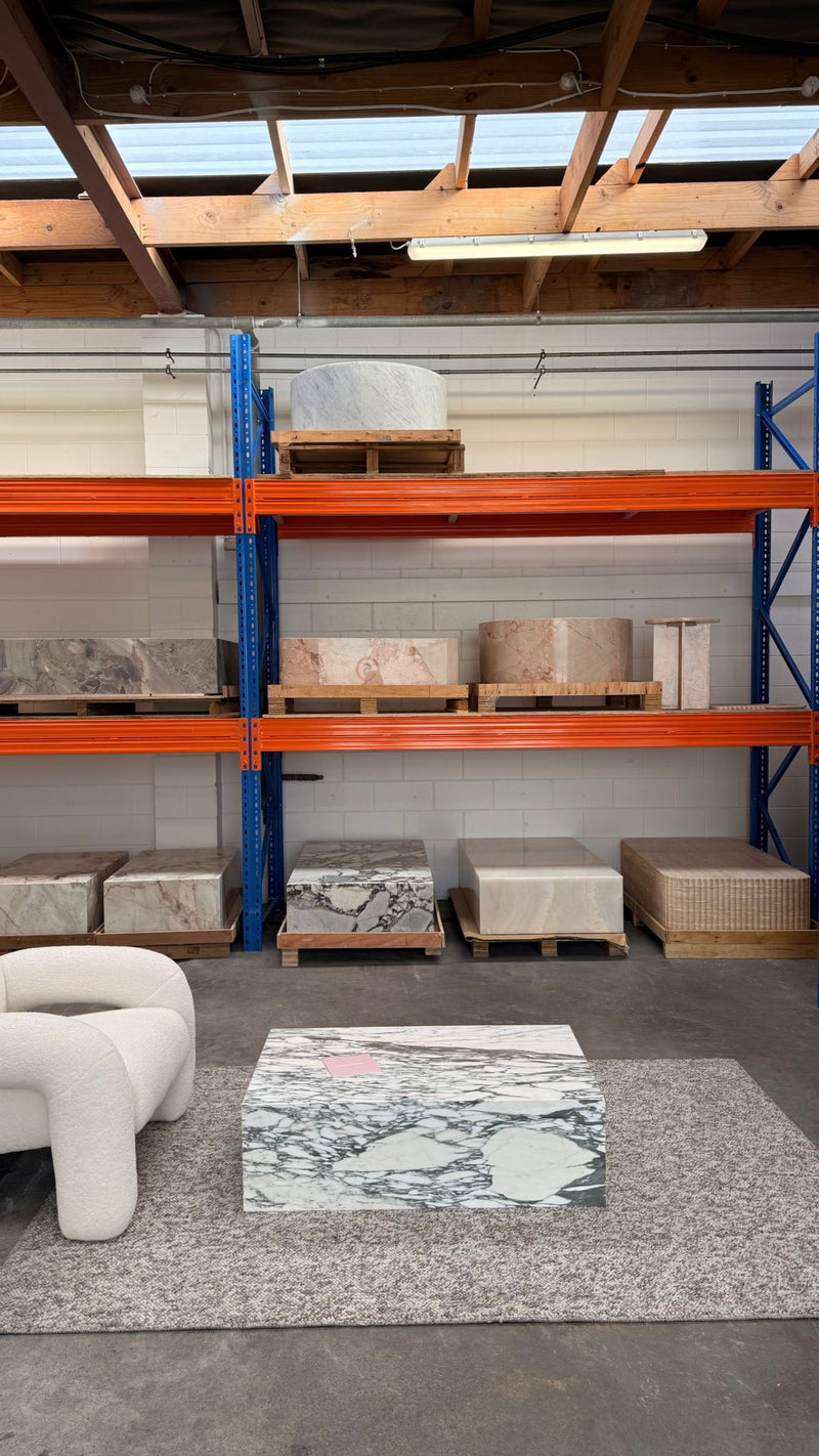 Natural Stone Co. showroom with marble coffee table, boucle armchair and stone furniture displayed on warehouse shelving.